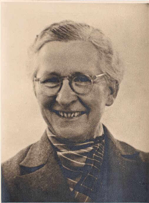 Black and white portrait of a smiling elderly woman with glasses.