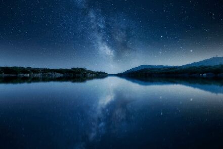 Starry night sky with Milky Way reflected on a calm lake.