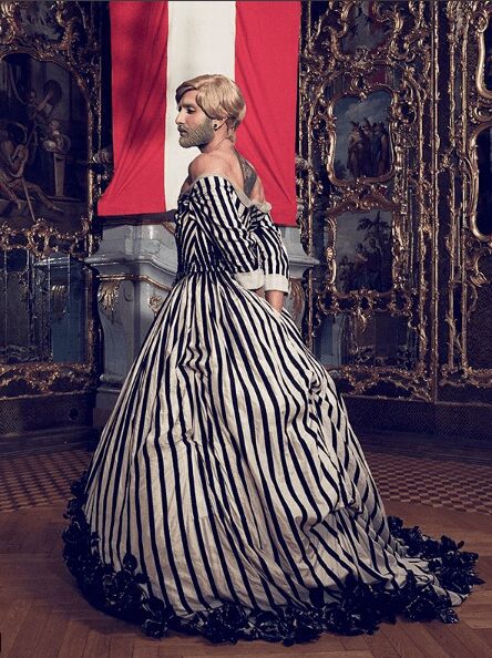 Woman in an elegant striped gown in a lavish, antique room.