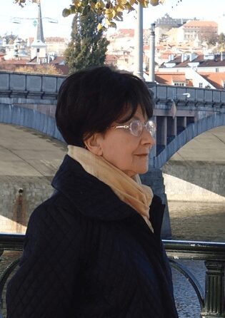 Profile of a woman wearing glasses and a scarf near a bridge.