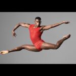 Ballet dancer in red leotard mid-leap.
