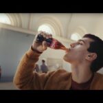 Person drinking from a Coca-Cola bottle.