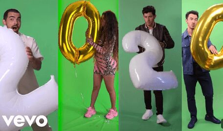Two people holding large inflatable numbers 0 and 2 against a green background.