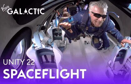 A man floats inside a spacecraft wearing a blue flight suit and sunglasses.