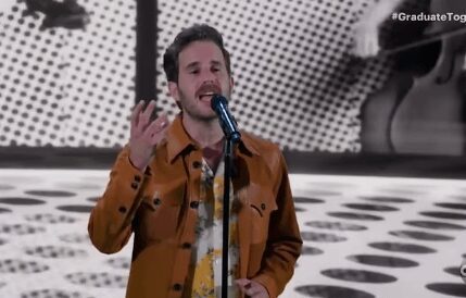 A man passionately singing into a microphone against a patterned backdrop.