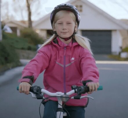 Young girl riding a bike in a residential neighborhood wearing a helmet and pink jacket.